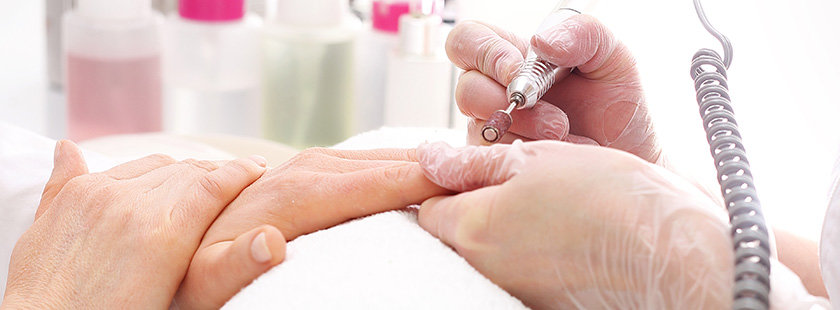 Kosmetyczka opracowuje paznokcie przy użyciu frezarki w salonie
